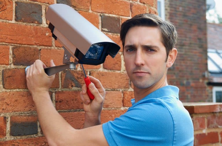 A tenant installing a surveillance camera on a brick wall for security purposes.