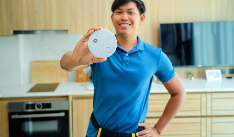 Man smiling and holding a carbon monoxide alarm in a modern kitchen in a rental property.