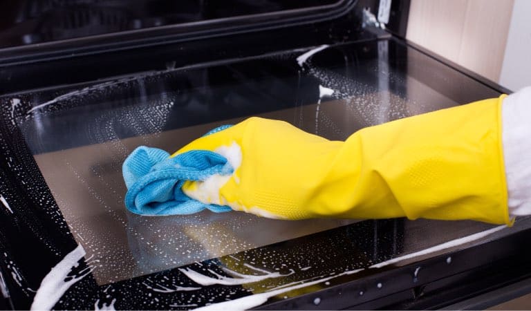 A person cleaning an oven with a yellow glove in rental property.