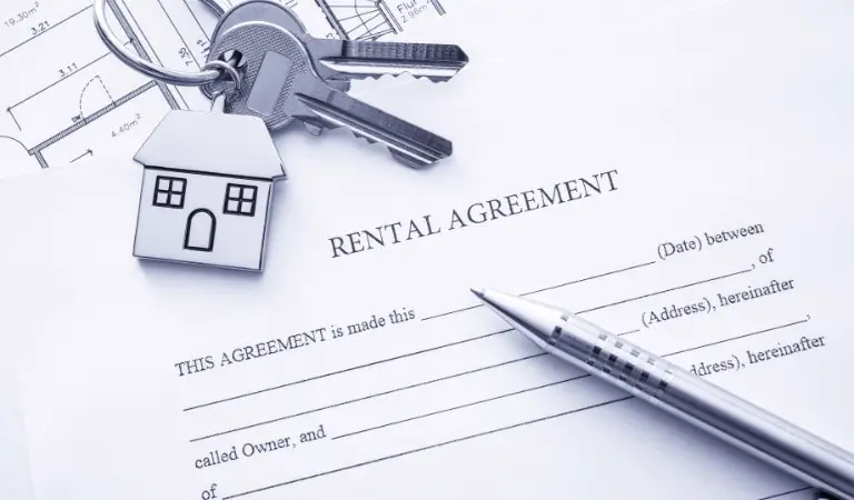 A set of keys and a house-shaped keychain rest on top of a rental agreement document, alongside a silver pen, indicating the preparation for a real estate transaction or tenancy agreement signing.